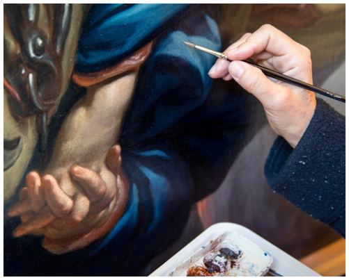 Artist skillfully restoring an antique painting with a fine paintbrush