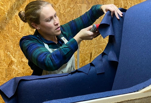 gem-working Gemma Broad, an upholsterer, adding blue woollen fabric onto a modern armchair.