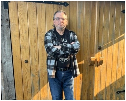 Conrad Langworthy, a toy restorer, standing in front of the double wooden doors of his workshop.