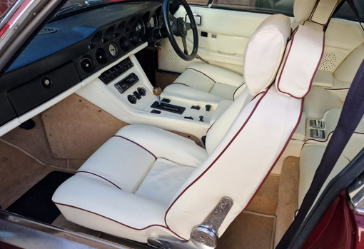 Cream leather car seat with contrast red piping in a car interior.