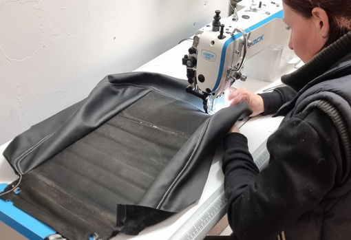 Woman sewing black leather car upholstery seats on an industrial sewing machine.