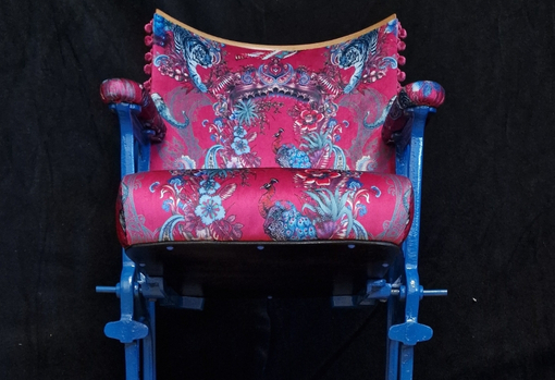 Vintage cinema seat newly reupholsteres in a red and blue patterned fabric with painted blue legs.
