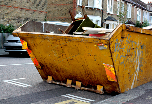 Furniture dumped in skip a yellow rubbish skip sitting on the side of the road with an armchair dumped in it